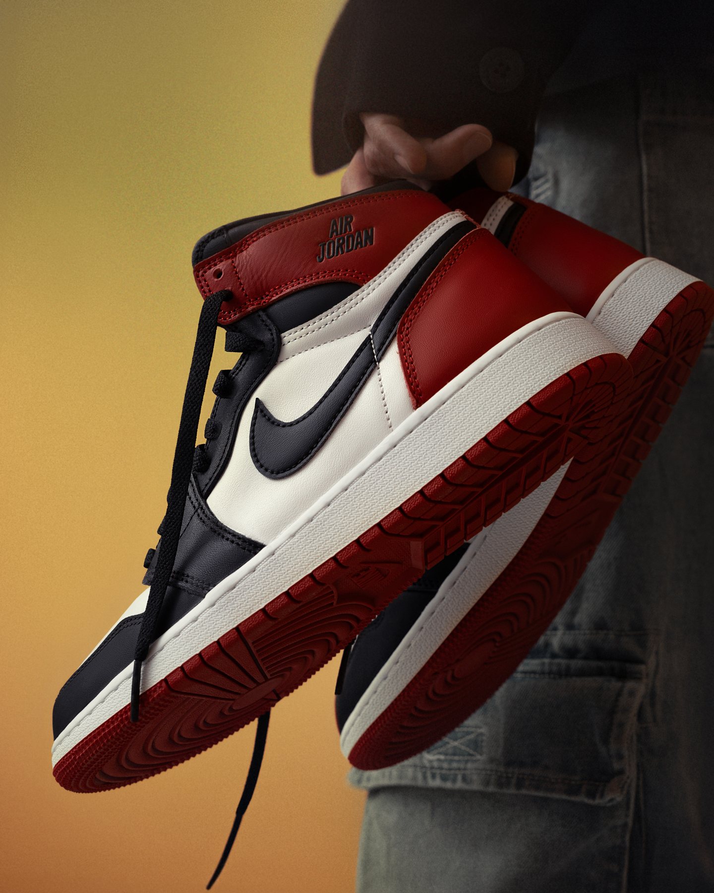 Sneaker shoot: Hand lifting the red pair against a warm yellow backdrop